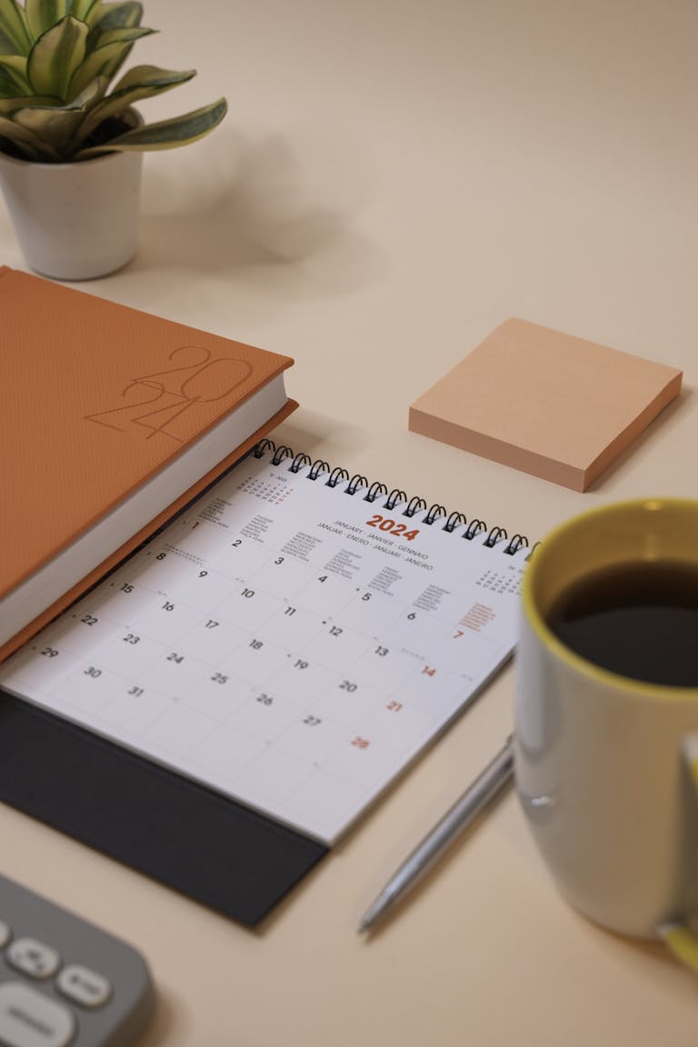 A 2024 calendar, notebook, and coffee on a peach-toned desk.