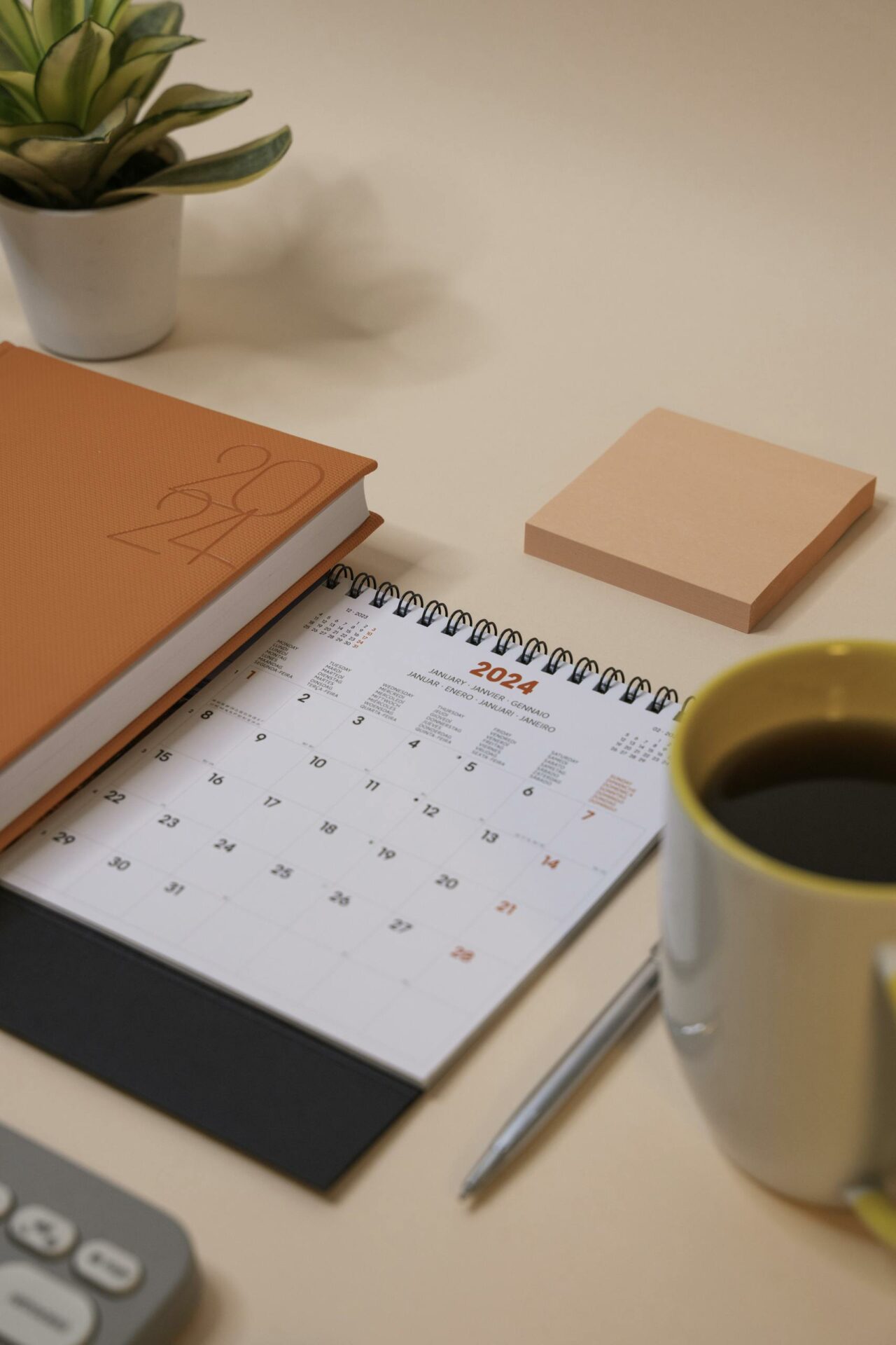 A 2024 calendar, notebook, and coffee on a peach-toned desk.