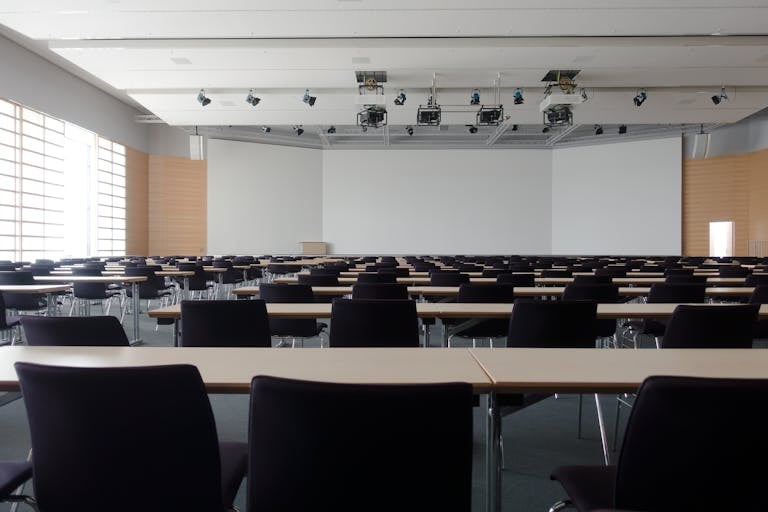 Spacious contemporary conference room with rows of tables and chairs, ready for meetings.