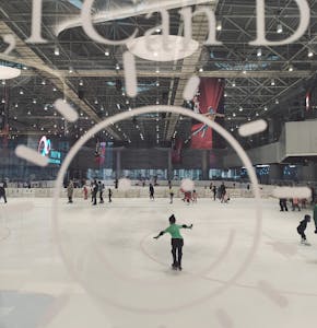 People ice skating at an indoor rink in Beijing with modern architectural design.